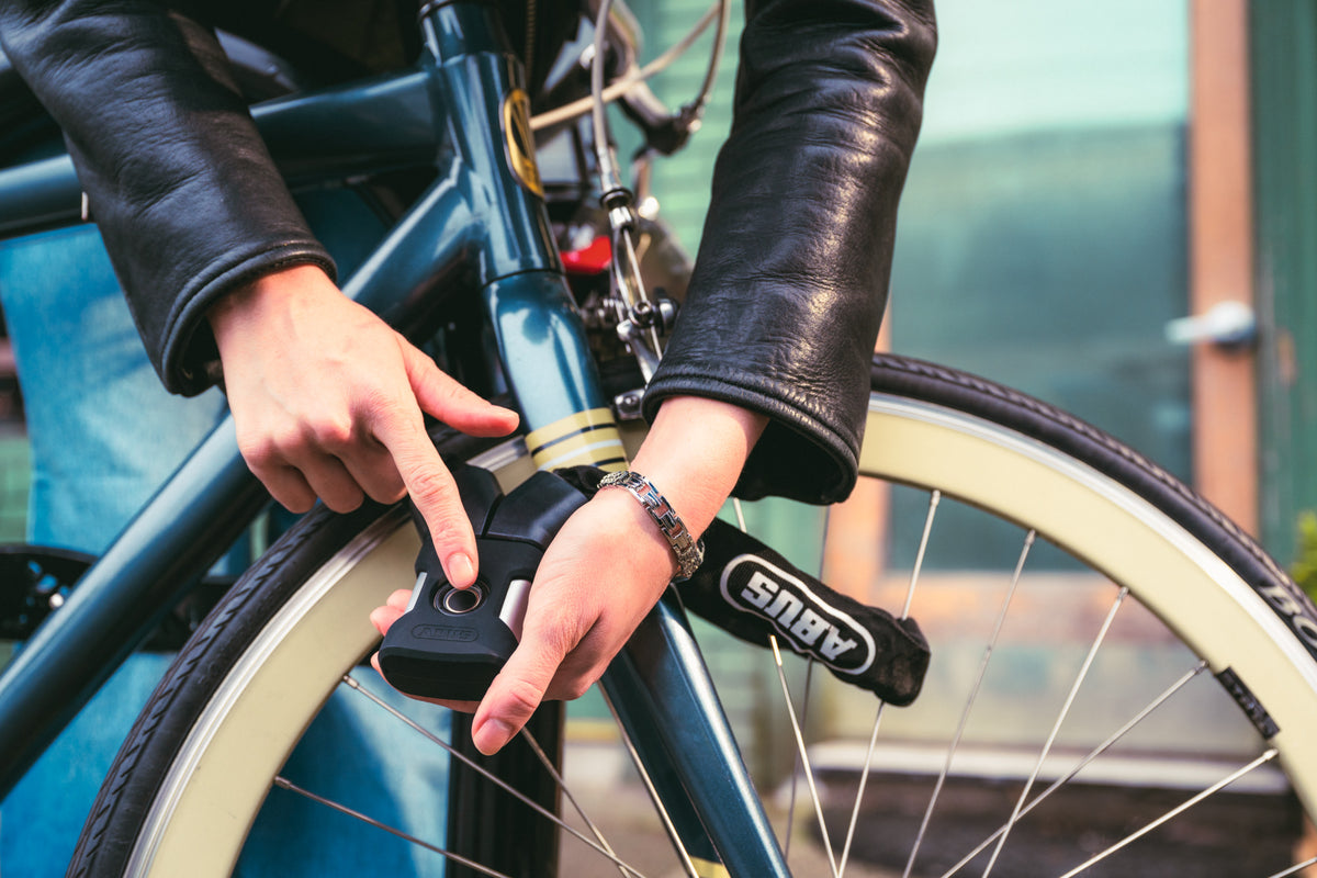 cyclist unlocking blue bicycle that is secured with ABUS ardo 7807F
