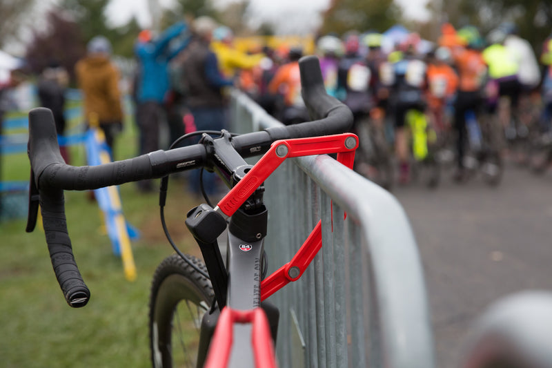 Load image into Gallery viewer, Red ABUS Bordo 6055K securing bicycle to fencing at bicycle race. #color_red
