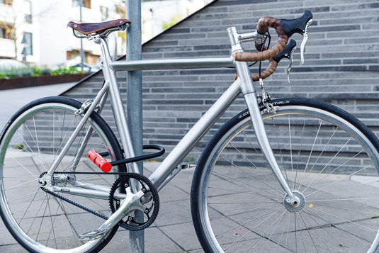 Silver bicycle locked to a pole with a brick wall background