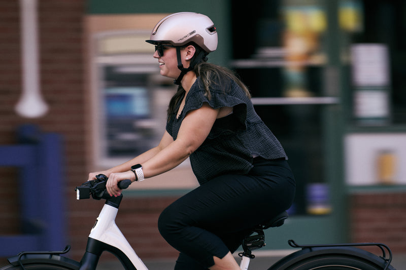 Load image into Gallery viewer, female cyclist riding white e-bike wearing champagne gold ABUS HUD-Y helmet #color_champagne gold
