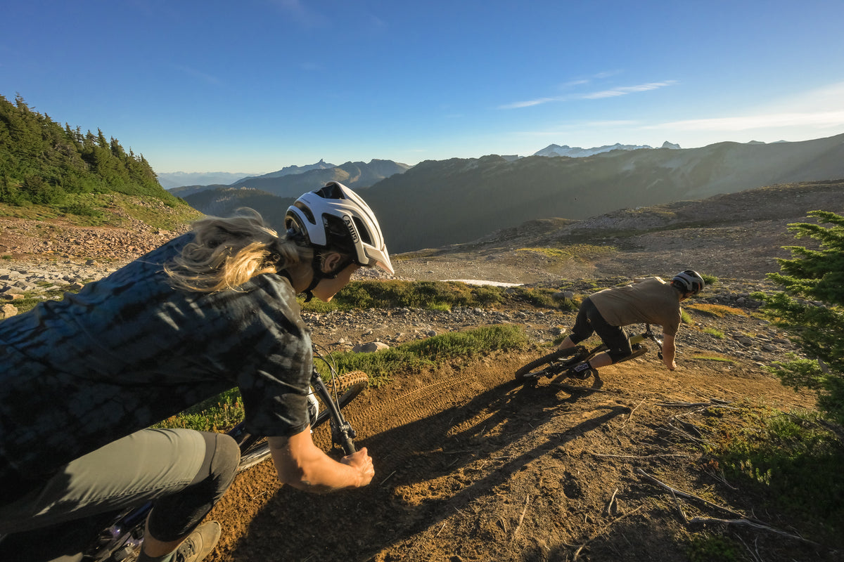 two cyclist riding down steep trail in mountains