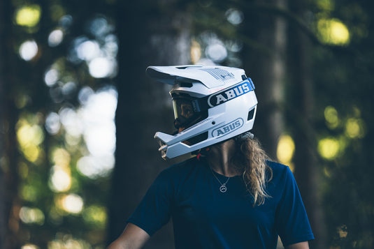 sitde profile of female cyclist standing in woods wearing ABUS HiDrop Helmet and ABUS Buteo goggles