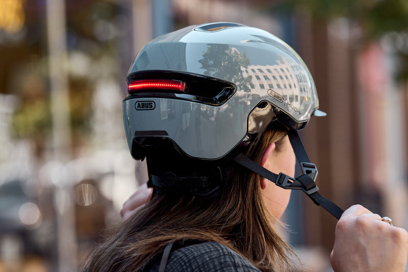 Load image into Gallery viewer, Cyclist putting on race grey ABUS HUD-Y helmet with light on #color_race grey
