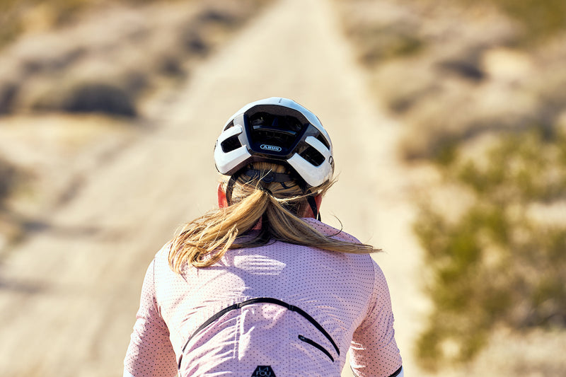 Load image into Gallery viewer, view from behind of female cyclist riding gravel road and wearing white ABUS PowerDome helmet #color_shiny white

